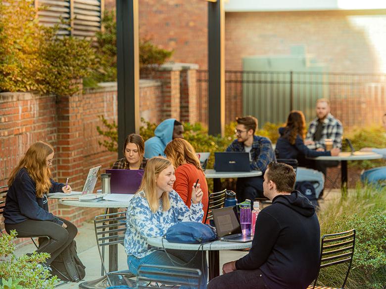 Campus courtyard with students seated around tables and taking in some sun